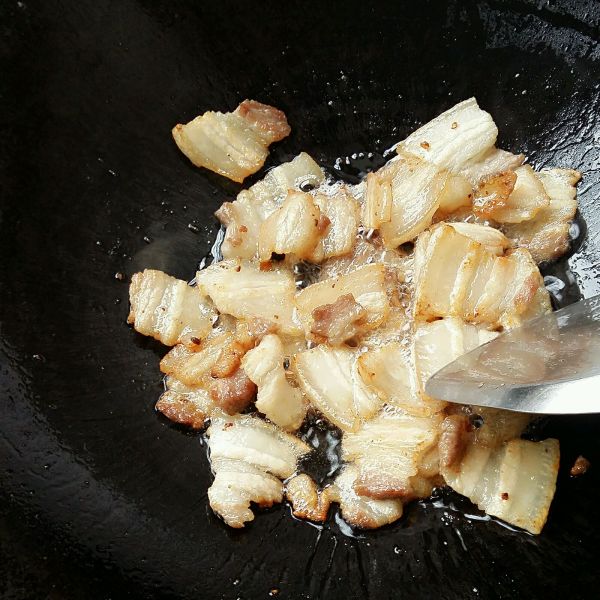 五花肉炒蒜苔的做法操作步骤第3步：倒入五花肉小火煸出油脂，煸至五花肉焦黄烹入料酒。（如果油太多可以盛出一些。）
