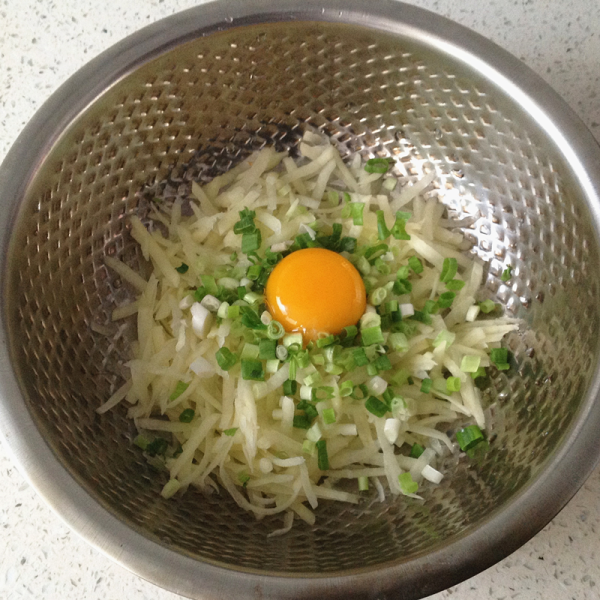 土豆丝软饼红豆粥的做法操作步骤第2步：往土豆丝中打入一个鸡蛋， 放入适量的葱花和盐。