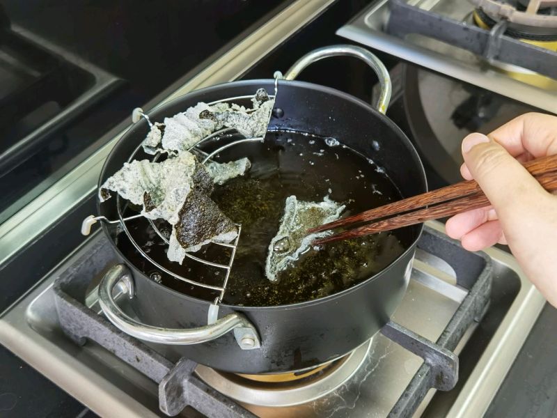咸蛋黄海苔脆的做法操作步骤第6步：油温180一190℃，用筷子定形，让它卷起来，不定形也行，就是一片平的，不介意形状的话可忽略。炸3一5秒即可。用厨房用纸吸收多余油脂。