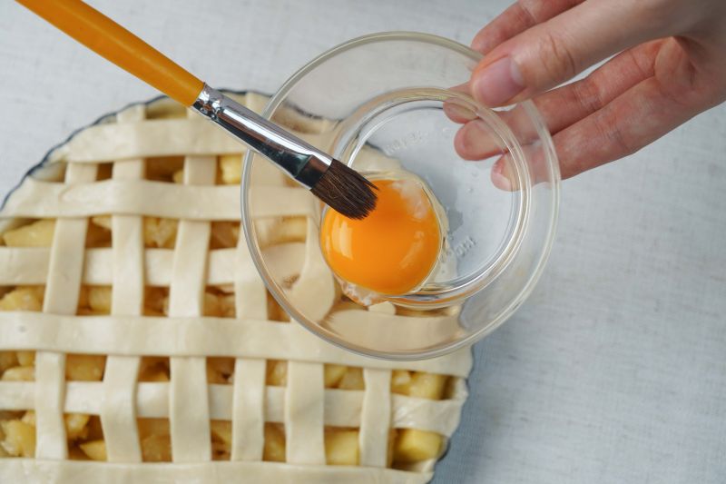 酥皮苹果派的做法操作步骤第12步：打入一个蛋黄，用笔刷沾取均匀的涂抹在手抓饼上