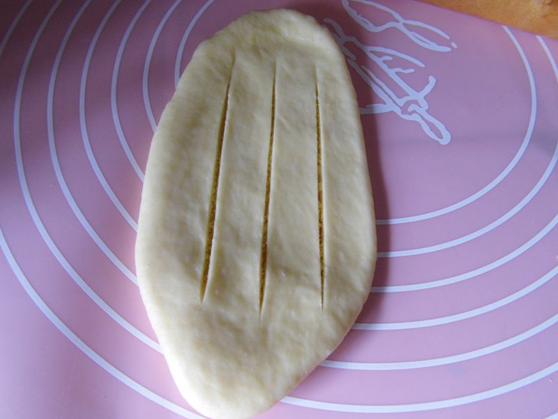 椰蓉面包的做法操作步骤第9步：用擀面杖擀成长牛舌状，用刀在表面划几刀
