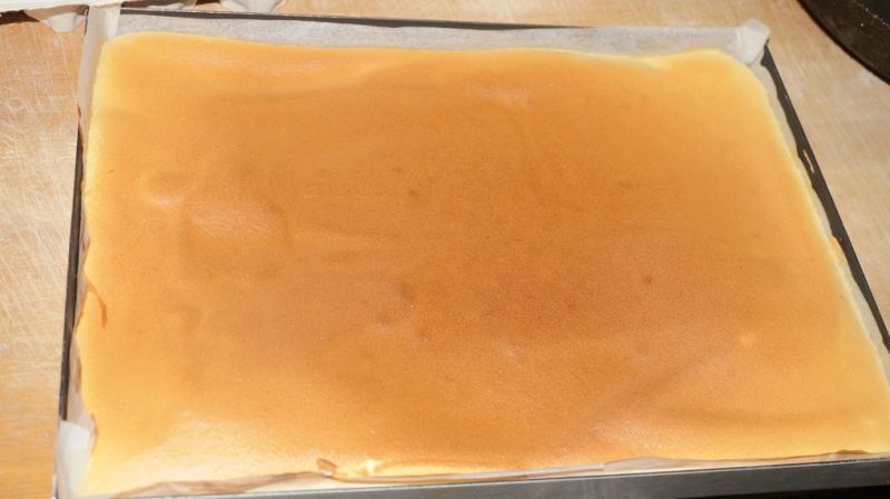 奶油戚风蛋糕卷的做法操作步骤第11步：出炉后，从烤盘中拖出，置于晾架上，将四周的油纸撕开，便于散热，表面盖一张干净油纸