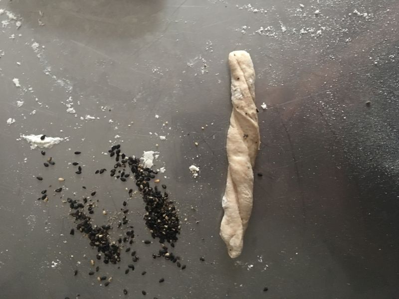 全麦椒盐芝麻咸面包棍——波兰种【健康小食】的做法操作步骤第7步：切割下来的面条，拉长旋转成螺纹，滚芝麻和现磨椒盐的混合物