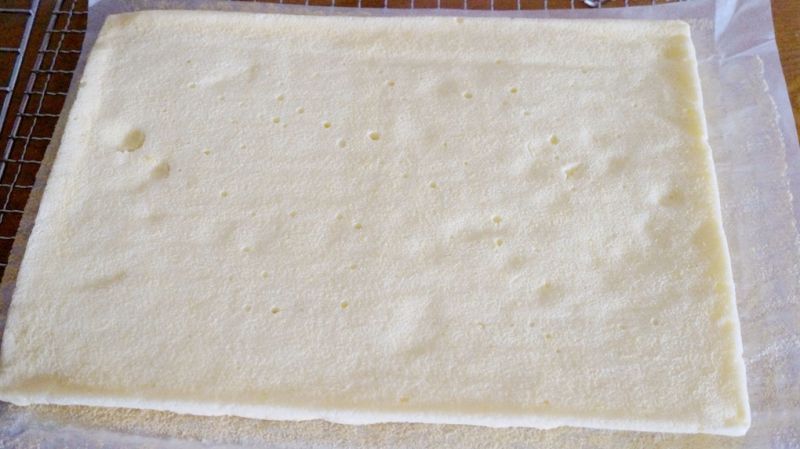 奶油戚风蛋糕卷的做法操作步骤第12步：5分钟之后，将蛋糕片翻面放置，并揭去底部的油纸，将其盖在蛋糕片表面