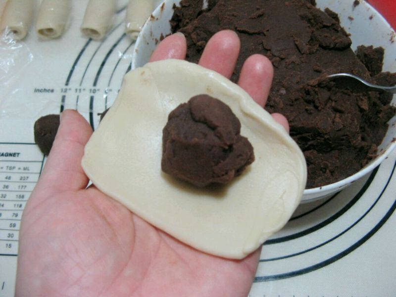红豆沙印花酥皮的做法操作步骤第14步： 取一个面卷，按扁，擀成近乎圆形；取适量的红豆沙馅放在皮子中间