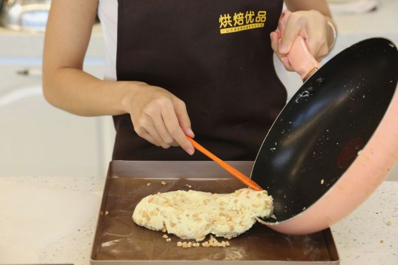 花生牛轧糖的做法操作步骤第6步：糖胚倒入不粘锅盘内，用高温布或者软硅胶垫揉搓数分钟，压平表面