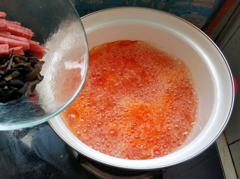 懒人开胃酸辣汤，西红柿的另类打开方式的做法操作步骤第9步：水开以后倒入火腿肠丝和木耳丝。