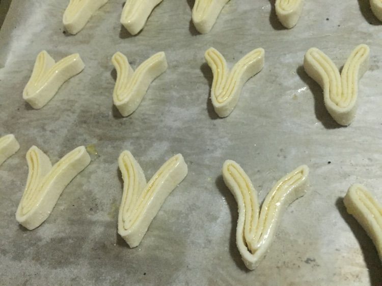 蝴蝶酥的做法操作步骤第5步：再叠起来，切成半厘米左右的厚度。放在烤盘上，把两边稍微向外掰开，类似Y的形状。以便膨胀起来形成美丽的蝴蝶形。再双面涂上黄油。